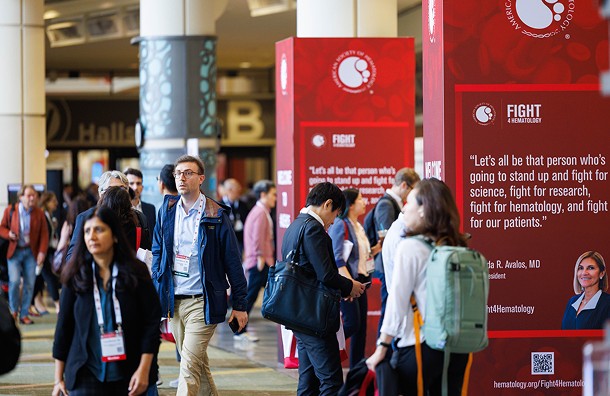 People walk and converse in front of Fight4Hematology signage at the annual meeting