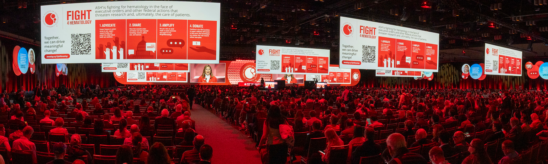 A photo of a Stage banner featuring the Fight 4 Hematology  slide at the ASH annual meeting with people in attendance