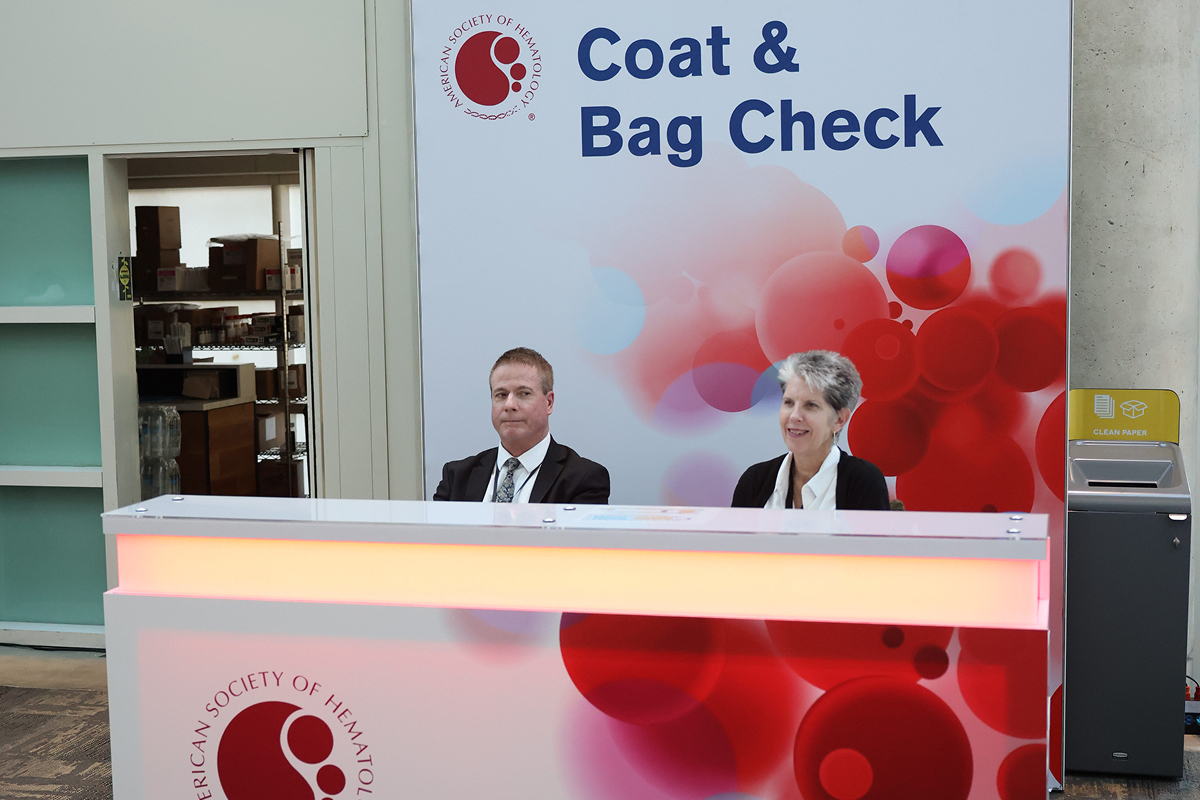 A man and a woman are at the coat and bag check front desk during the ASH annual meeting.